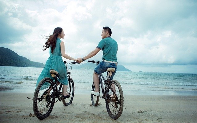 Muž a žena na bicykloch na pláži sa držia za ruky.jpg
